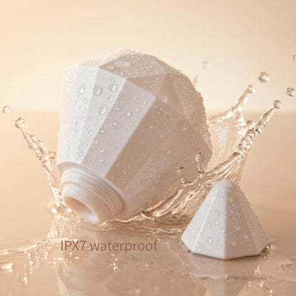 Pearl-white diamond-shaped wellness device displayed with clear water droplets on a soft beige background, representing waterproof performance and premium hygiene
