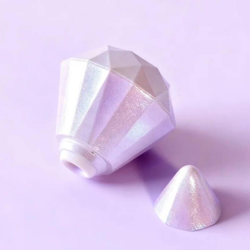 Overhead view of an elegant pearl-white diamond clitoral sucker with the cap open, resting on a soft lavender background with an iridescent glow. A luxury aesthetic pleasure accessory.